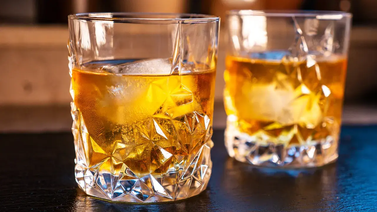 Zwei Gläser mit bernsteinfarbenem on the rocks drink, Eiswürfel schmelzen langsam.