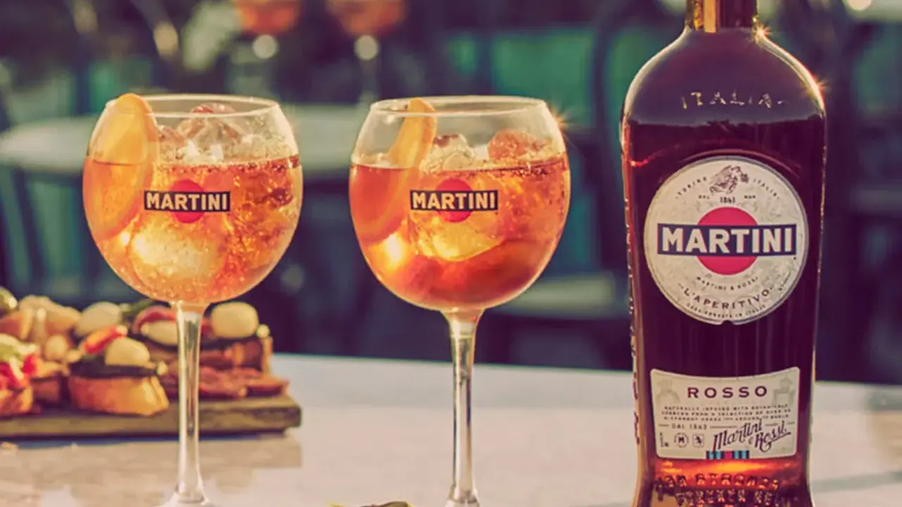 Zwei Gläser Martini mit Eis und Orangenscheibe, daneben eine Flasche Martini Rosso. Perfekt für den Aperitif, mit dem richtigen Martini prozent.