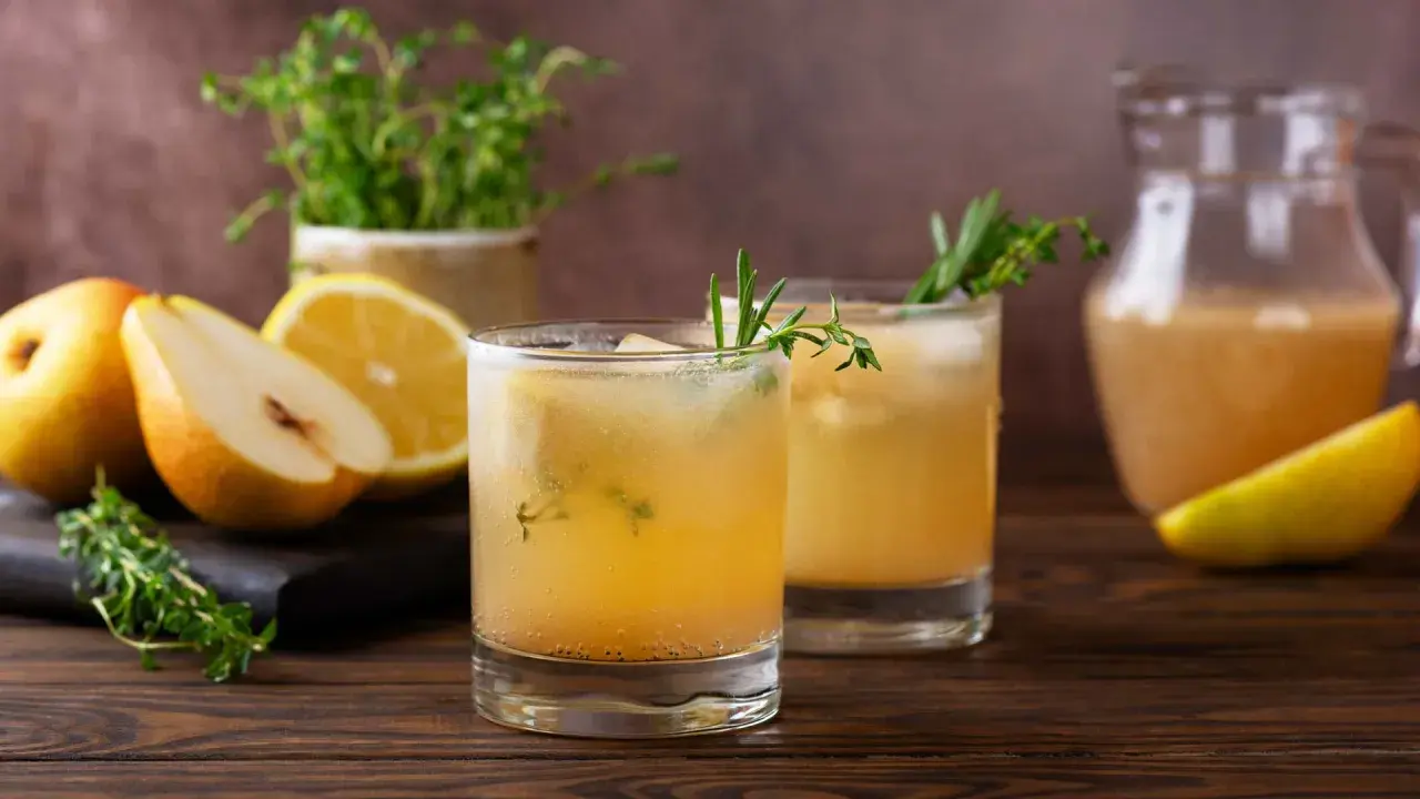Erfrischender birnen spritz mit Zitrone und Kräutern, serviert mit frischen Früchten und einem Krug des Getränks.