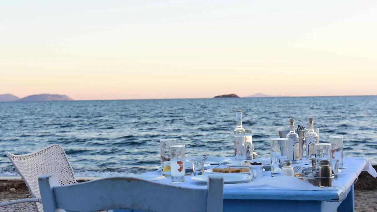 Tisch am Meer mit Ouzo-Flaschen, Gläsern und Essen. Der Ouzo-Prozent ist perfekt für den Sonnenuntergang.