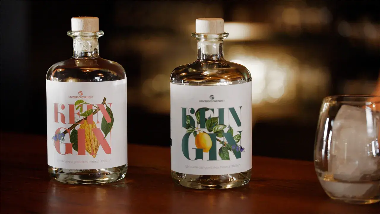 Zwei Flaschen "Rein Gin" mit Holzkorken stehen bereit zur **Gin Aufbewahrung**. Daneben ein Glas mit Eiswürfeln.