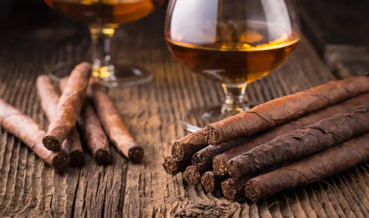 Zwei Gläser Cognac und Zigarren auf Holztisch. So trinkt man Cognac: langsam und genussvoll.