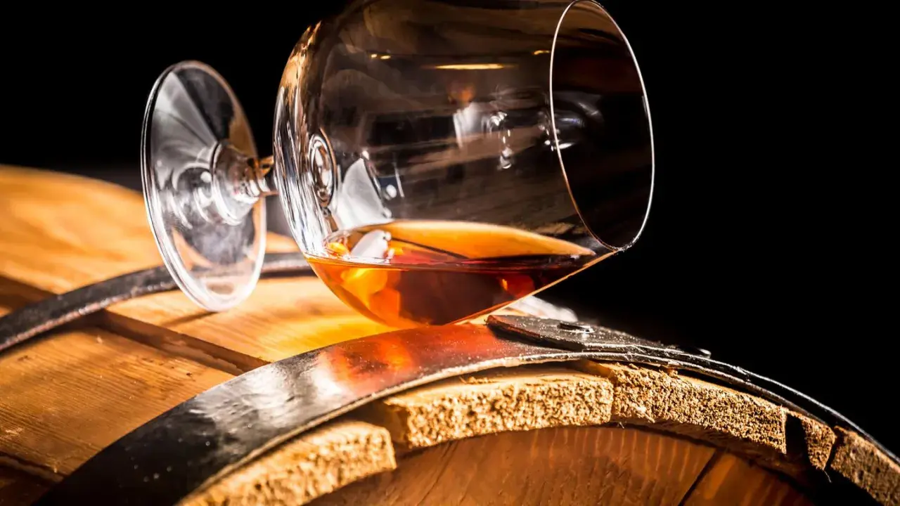 Ein Glas bernsteinfarbener Brandy ruht auf einem Holzfass. So sieht aus, was ein Brandy ist: ein edler Tropfen.