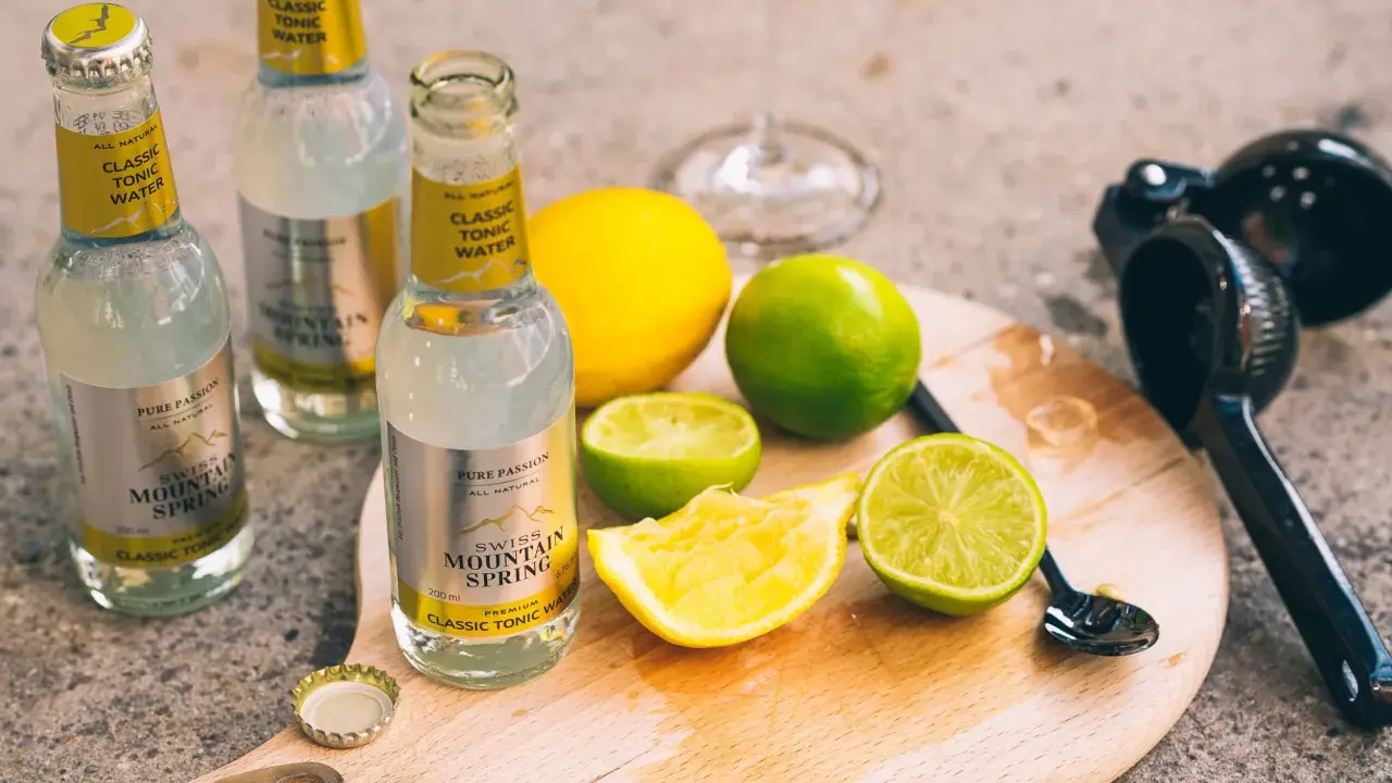 Flaschen mit "Classic Tonic Water", Zitronen- und Limettenspalten auf einem Holzbrett. Die Bedeutung von Gin & Tonic wird hier durch die Zutaten für einen perfekten Drink unterstrichen.