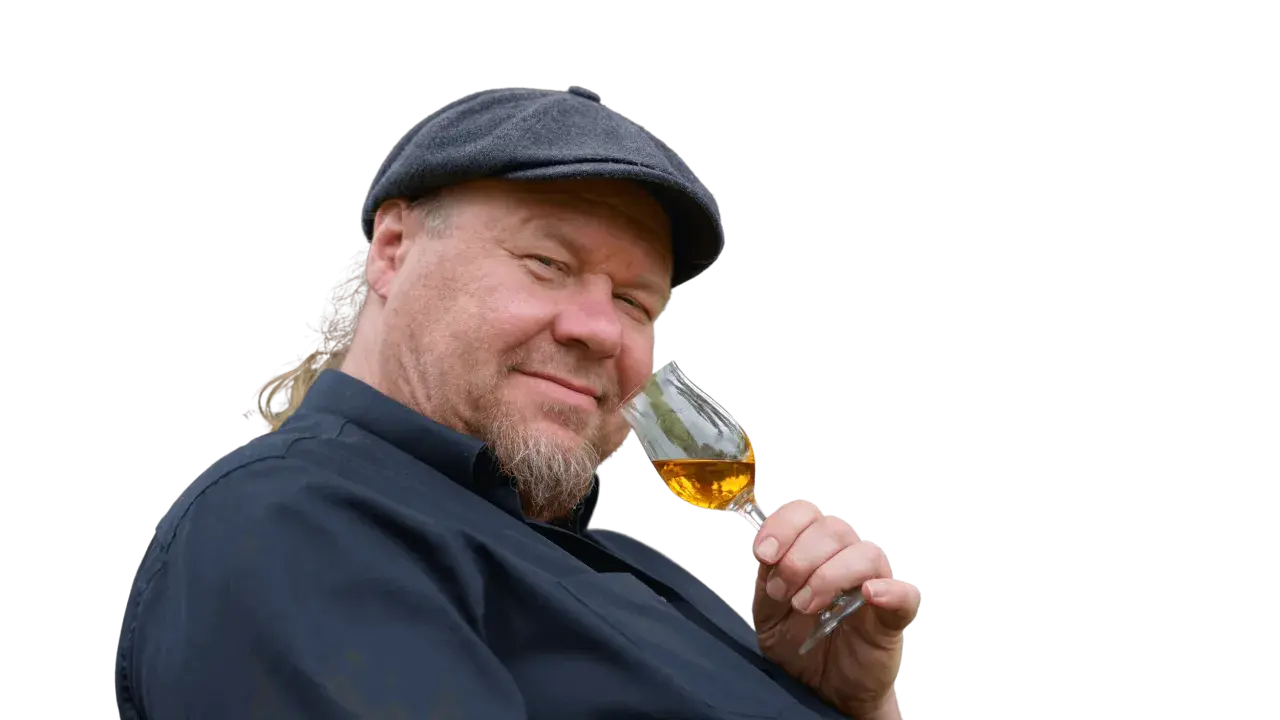 Ein Mann mit Schiebermütze und Bart hält ein Glas bernsteinfarbenen Rum. Er scheint zu wissen, wie man Rum genießt.