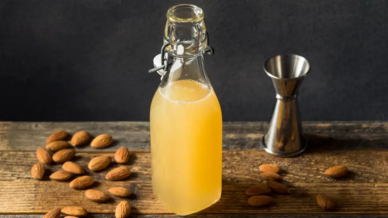 Flasche mit selbstgemachtem Mandelsirup, umgeben von Mandeln und einem Messbecher. Perfekt, um Mandelsirup selber zu machen!