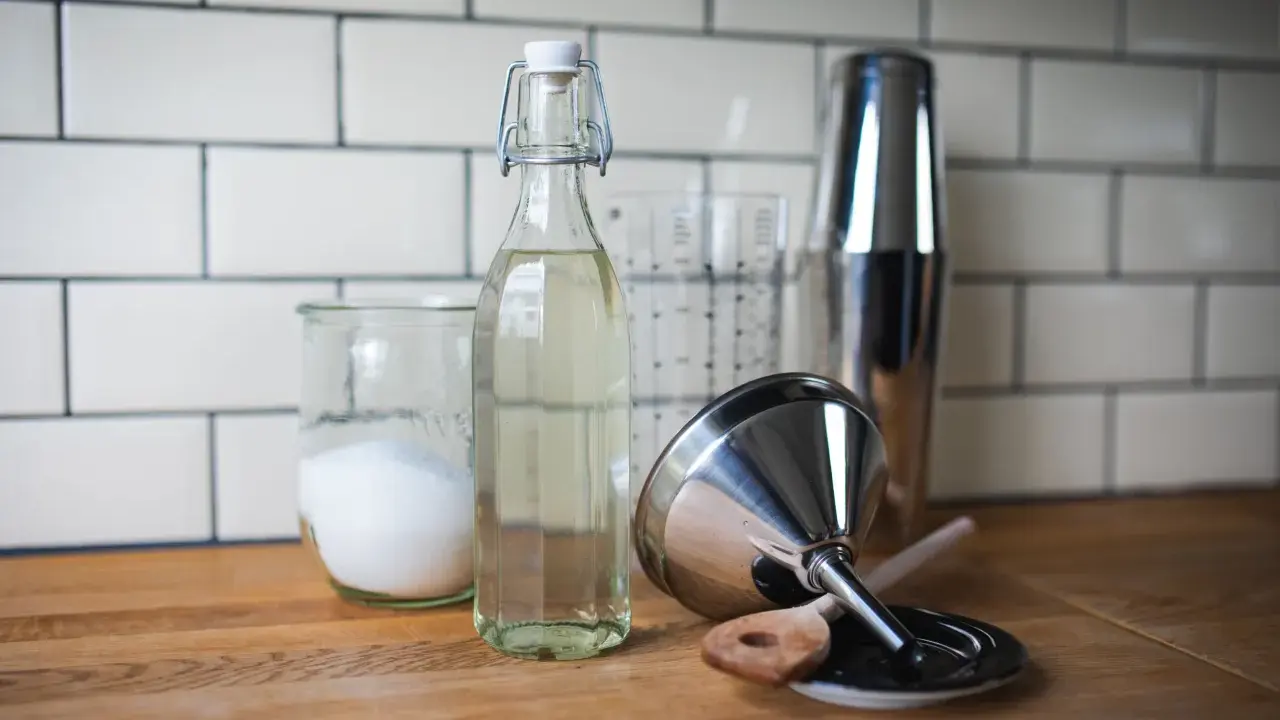 Zutaten für zuckersirup selber machen: Zucker in einem Glas, eine Flasche Sirup, ein Messbecher und ein Cocktailshaker.