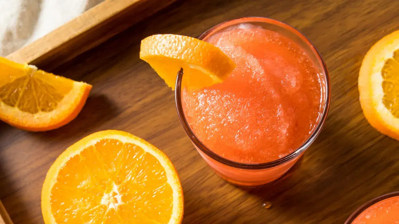 Gefrorene Aperol Spritz Varianten mit frischen Orangenscheiben auf Holztisch.