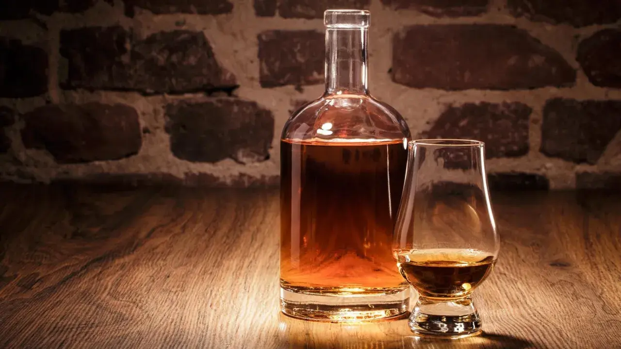 Eine Karaffe und ein Glas mit bernsteinfarbenem Whisky vor einer Ziegelwand. Verschiedene Whisky-Sorten laden zum Genuss ein.