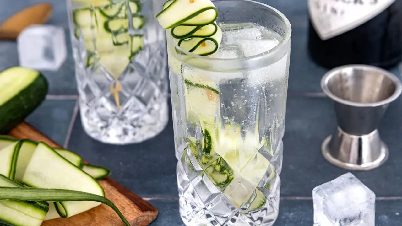 Erfrischendes Gin Tonic Rezept mit Gurke: Eisgekühlte Gläser, frische Gurkenscheiben und eine Flasche Gin.