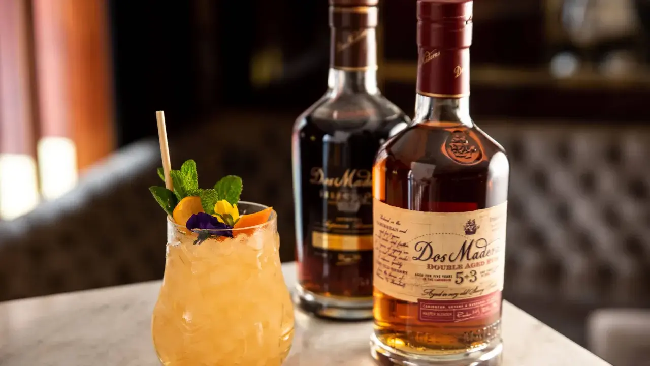 Ein erfrischender Cocktail mit Minze und Früchten neben zwei Flaschen Dos Maderas Rum. Der Alkoholgehalt des Rums ist auf dem Etikett angegeben.