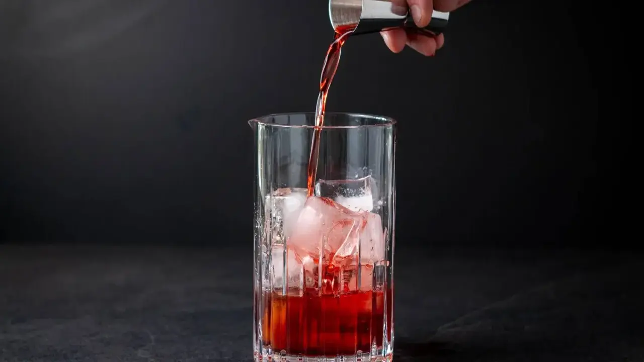 Ein Barkeeper gießt Campari Gin mit Eis in ein Glas.