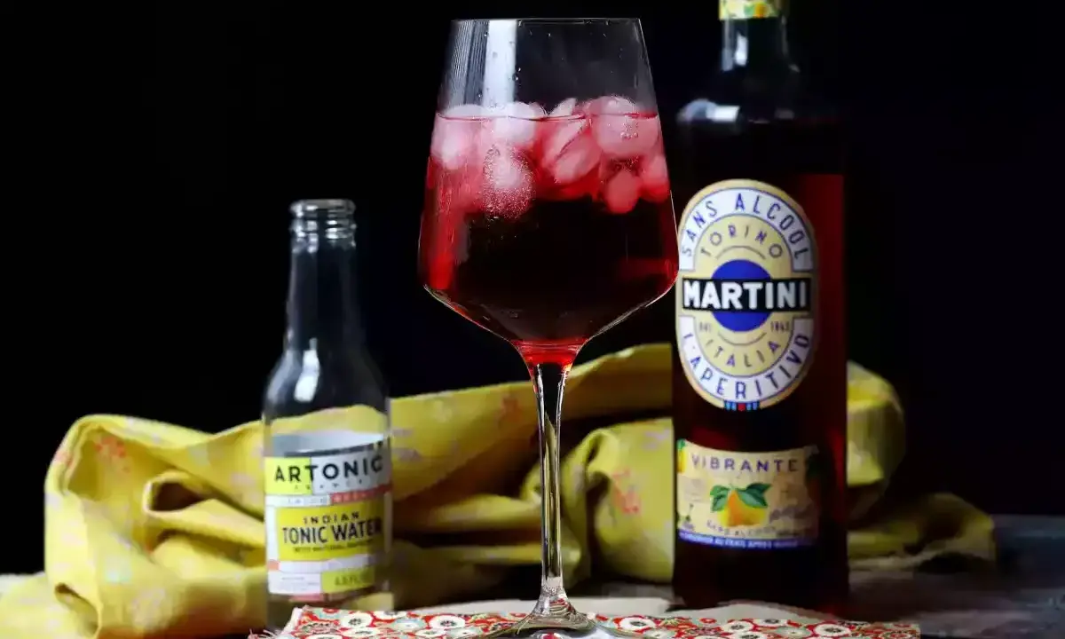 Ein Glas mit einem roten, eisgekühlten Getränk steht neben einer Flasche Martini alkoholfrei und Tonic Water.