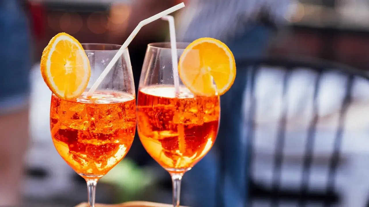 Zwei Aperol Spritz mit Orangenscheiben und Strohhalmen. Der leuchtende Aperol Farbstoff schimmert in den Gläsern.