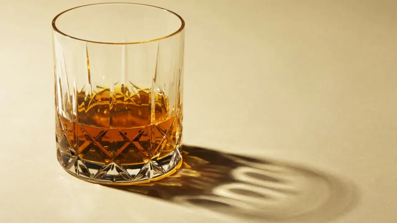 Ein Glas Whisky mit starkem Schatten auf hellem Hintergrund.