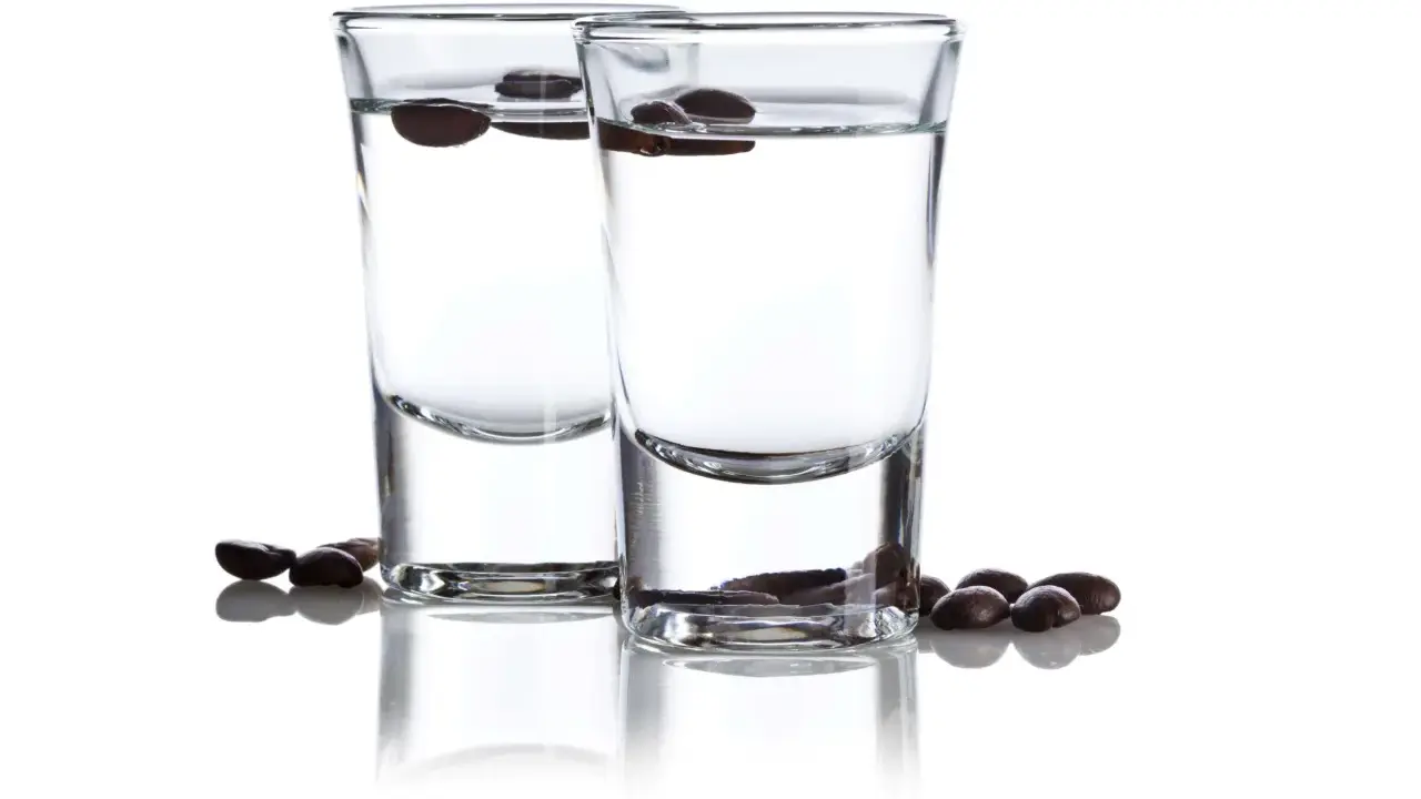 Zwei Gläser mit klarem Schnaps, darin schwimmende Kaffeebohnen. Der Sambuca-Prozent ist hier gut sichtbar.
