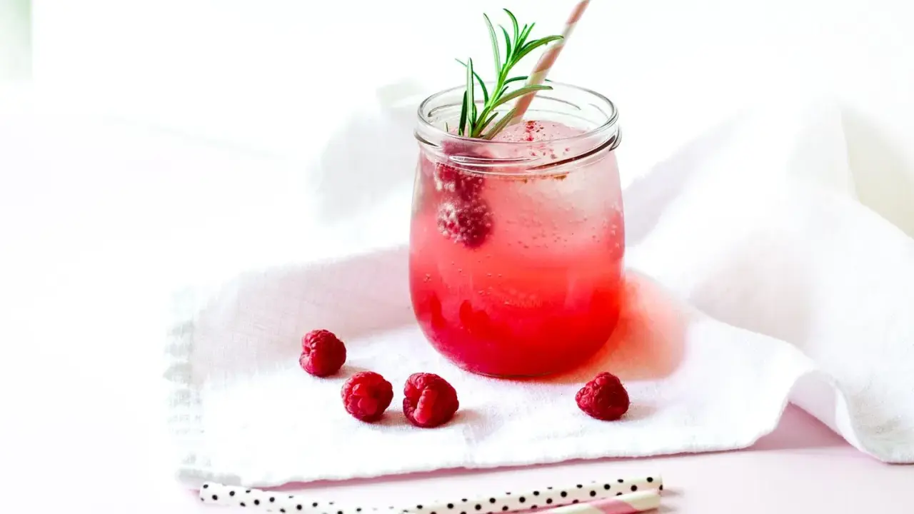 Erfrischender Gin Tonic mit Himbeeren, garniert mit Rosmarin. Ein süßer Genuss an einem warmen Tag.