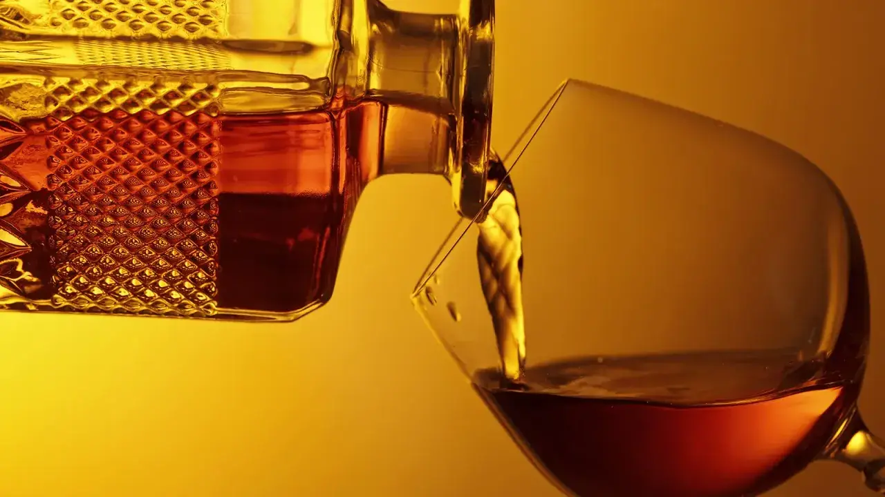 Bernsteinfarbener Armagnac fließt aus einer Karaffe in ein Glas. Was ist das? Ein edler Weinbrand aus Frankreich.