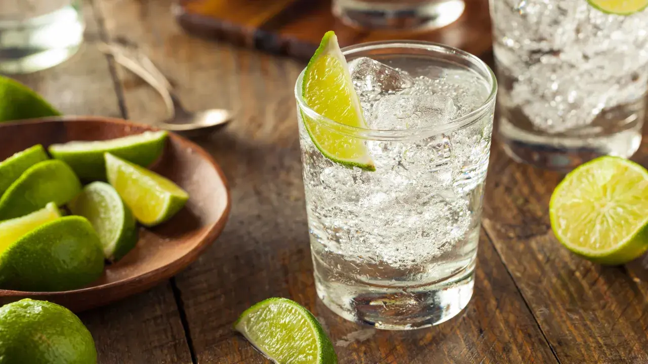 Erfrischender infused gin mit Eis und Limettenspalten auf rustikalem Holztisch.