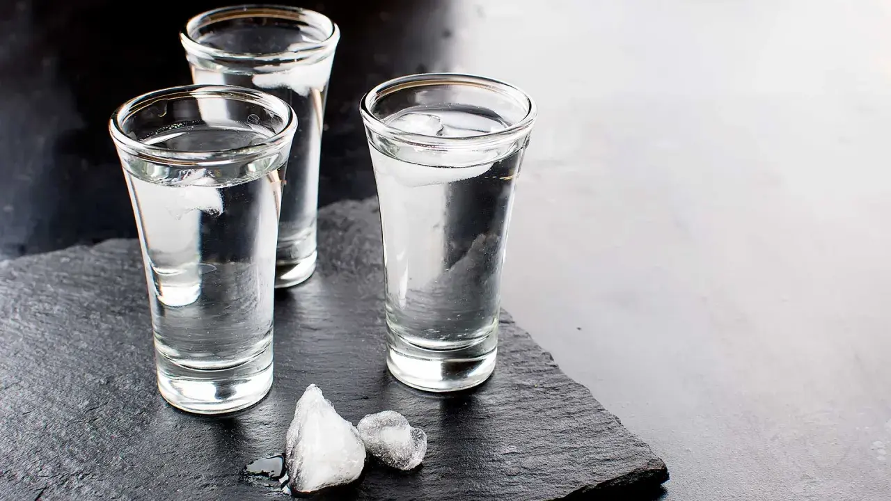 Drei Gläser Wodka mit Eiswürfeln auf schwarzem Schiefer. Wodka wird aus Getreide oder Kartoffeln hergestellt.