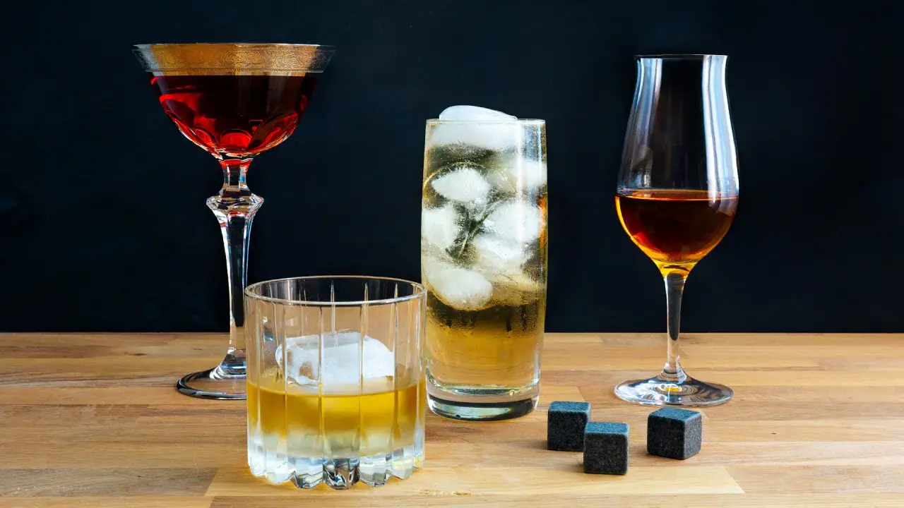 Vier Gläser mit verschiedenen Getränken, darunter ein Glas mit peated whisky, Eiswürfel und Whiskysteine auf Holztisch.