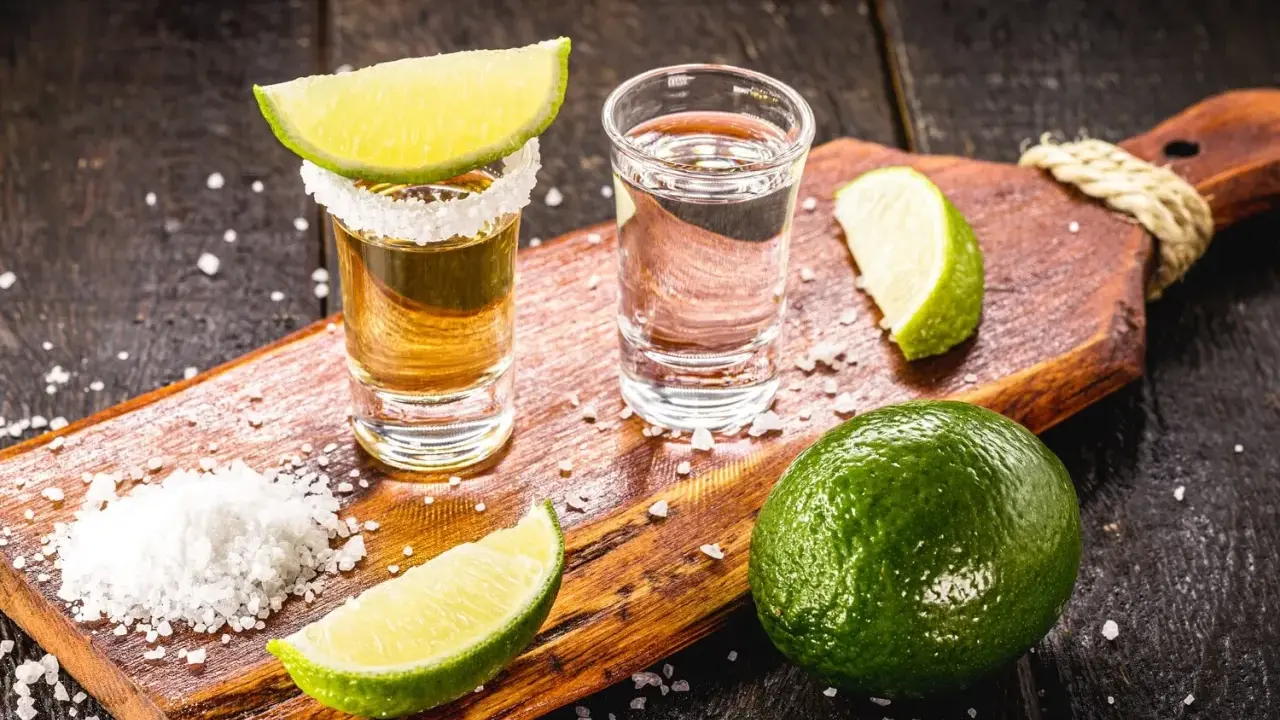 Zwei Gläser Tequila, eines mit Salzrand und Limettenspalte, daneben Salz und Limetten. Perfekt zum Tequila trinken.
