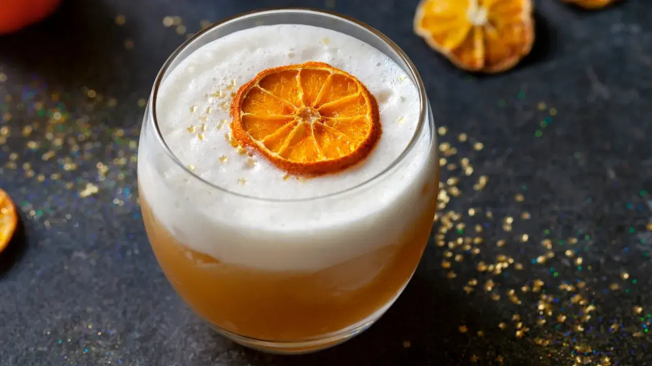Ein cremiger Amaretto Cocktail mit einem getrockneten Orangenscheibchen und goldenem Glitzer.
