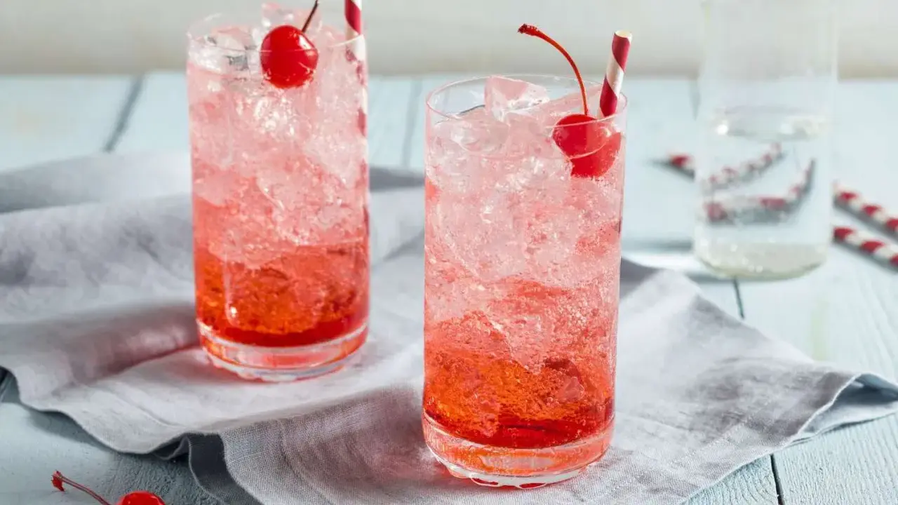 Zwei erfrischende Getränke mit Eis, Kirschen und Strohhalmen. Die rote Farbe verrät, was ist Grenadine: ein süßer Sirup aus Granatäpfeln.
