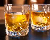 Zwei Gläser mit bernsteinfarbenem on the rocks drink, Eiswürfel schmelzen langsam.