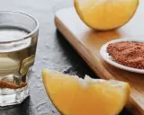 Ein Glas Tequila mit Wurm, daneben Orangenstücke und eine Schale mit Gewürzmischung.