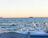 Tisch am Meer mit Ouzo-Flaschen, Gläsern und Essen. Der Ouzo-Prozent ist perfekt für den Sonnenuntergang.