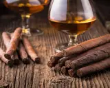 Zwei Gläser Cognac und Zigarren auf Holztisch. So trinkt man Cognac: langsam und genussvoll.