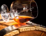 Ein Glas bernsteinfarbener Brandy ruht auf einem Holzfass. So sieht aus, was ein Brandy ist: ein edler Tropfen.
