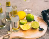 Flaschen mit "Classic Tonic Water", Zitronen- und Limettenspalten auf einem Holzbrett. Die Bedeutung von Gin & Tonic wird hier durch die Zutaten für einen perfekten Drink unterstrichen.
