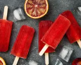 Erfrischende Eis am Stiel mit Campari Orange Geschmack, umgeben von Eiswürfeln und Blutorangen-Scheiben.