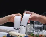 Zwei Hände stoßen mit Gläsern voller weißem Raki an. So trinkt man Raki: langsam, mit Freunden und gutem Essen.