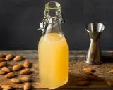 Flasche mit selbstgemachtem Mandelsirup, umgeben von Mandeln und einem Messbecher. Perfekt, um Mandelsirup selber zu machen!