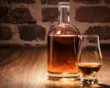 Eine Karaffe und ein Glas mit bernsteinfarbenem Whisky vor einer Ziegelwand. Verschiedene Whisky-Sorten laden zum Genuss ein.