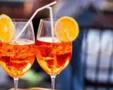 Zwei Aperol Spritz mit Orangenscheiben und Strohhalmen. Der leuchtende Aperol Farbstoff schimmert in den Gläsern.
