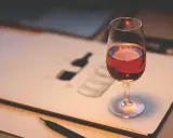 Ein Glas Portwein steht auf einem Skizzenbuch, das eine Flasche zeigt. Perfekt, um zu lernen, wie trinkt man Portwein.