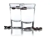 Zwei Gläser mit klarem Schnaps, darin schwimmende Kaffeebohnen. Der Sambuca-Prozent ist hier gut sichtbar.