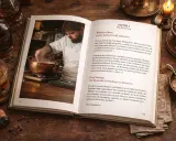Ein Koch bereitet etwas in einem Kupfertopf zu, während ein Buch über die richtige trinktemperatur whisky daneben liegt.