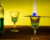 Grüner Absinth brennt in einem Glas, ein Zuckerwürfel karamellisiert. Die Zubereitung erinnert an die traditionelle Absinth Herkunft.