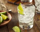 Erfrischender infused gin mit Eis und Limettenspalten auf rustikalem Holztisch.