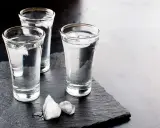 Drei Gläser Wodka mit Eiswürfeln auf schwarzem Schiefer. Wodka wird aus Getreide oder Kartoffeln hergestellt.