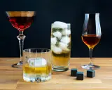 Vier Gläser mit verschiedenen Getränken, darunter ein Glas mit peated whisky, Eiswürfel und Whiskysteine auf Holztisch.