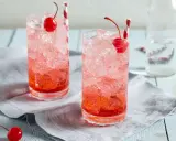 Zwei erfrischende Getränke mit Eis, Kirschen und Strohhalmen. Die rote Farbe verrät, was ist Grenadine: ein süßer Sirup aus Granatäpfeln.