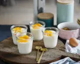 Vier Gläser mit cremigem Dessert, garniert mit Orangenspalten, ideal für Cointreau Rezepte. Zwei goldene Löffel liegen daneben.