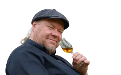 Ein Mann mit Schiebermütze und Bart hält ein Glas bernsteinfarbenen Rum. Er scheint zu wissen, wie man Rum genießt.