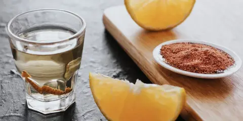 Ein Glas Tequila mit Wurm, daneben Orangenstücke und eine Schale mit Gewürzmischung.